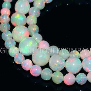 May include: A strand of white opal beads with iridescent rainbow colors. The beads are round and smooth, and they are strung on a clear thread. The beads are arranged in a circular pattern, and they are all of the same size.