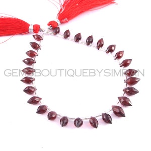 May include: A strand of 20 faceted, dark red gemstone beads, strung on silver wire. The beads are in a teardrop shape and are approximately 10mm in length. The strand is finished with red tassels on each end.