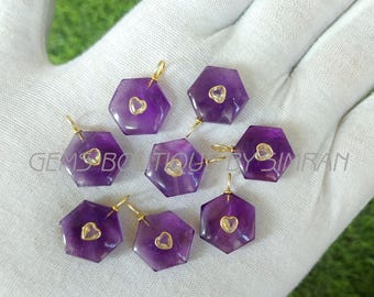 May include: Seven hexagonal amethyst pendants with gold-colored bails and heart-shaped accents. The pendants are a deep purple color and are displayed on a white surface. The text "GEMS BOUTIQUE BY SIMRAN" is visible.