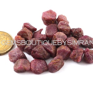 Pode incluir: Um monte de pedras preciosas de rubi vermelho bruto. As pedras preciosas são de vários tamanhos e formas. Uma pequena moeda australiana está incluída para escala.