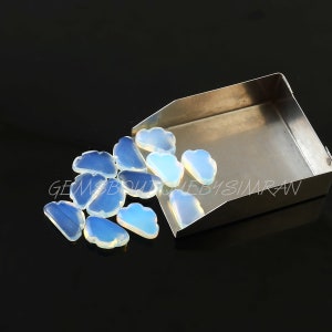 May include: A group of 12 iridescent opal cabochons in a cloud shape. The cabochons are a pale blue colour with a slight iridescent sheen. The cabochons are arranged in a loose pile on a silver tray.