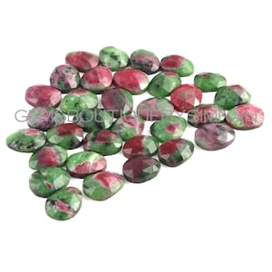 May include: A collection of 20 green and red oval-shaped gemstones. The gemstones have a faceted cut and are arranged in a pile.