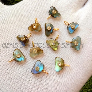 Puede incluir: Una colección de colgantes de piedras preciosas de labradorita con colgantes dorados. Cada colgante presenta una forma única y tonos iridiscentes azules, verdes y amarillos. Una pequeña gema transparente está engastada en el centro de cada colgante.