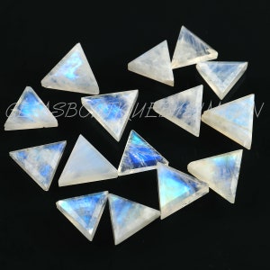May include: A collection of triangular moonstone gemstones. Each stone has a translucent white base with iridescent blue and rainbow flashes. The gemstones are arranged on a black surface, showcasing their unique shapes and colors.