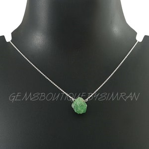May include: A silver chain necklace with a raw green gemstone pendant. The pendant is a rough, irregular shape and has a natural, unpolished look.