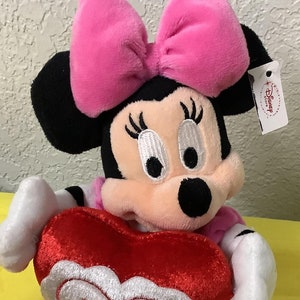 May include: Pink and black plush Minnie Mouse holding a red heart-shaped pillow with the text "You're the One" embroidered on it.