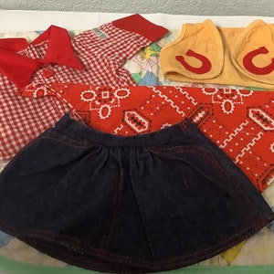 May include: A red and white checked shirt, a red bandana, a yellow waistcoat with red horseshoes, and a blue denim skirt. This is a doll outfit.