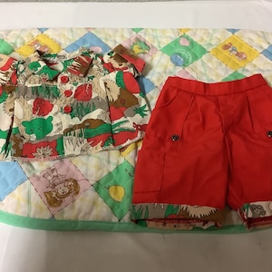 May include: A two-piece outfit for a child, featuring a short-sleeved shirt with a colourful animal print and red shorts with a matching print on the hem.