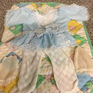 May include: A light blue baby doll dress with white lace trim and a white bow. The dress is paired with white tights and white socks.