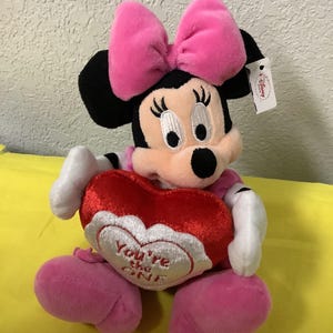 May include: A plush Minnie Mouse toy wearing a pink bow and holding a red heart-shaped pillow that says "You're My One".