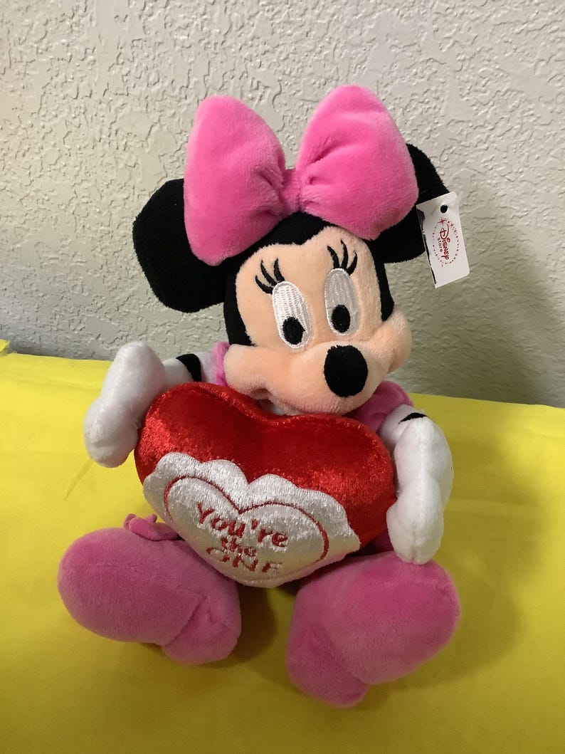 May include: A plush Minnie Mouse toy wearing a pink bow and holding a red heart-shaped pillow that says "You're My One".