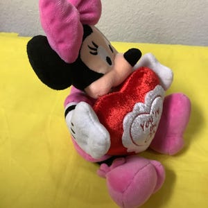May include: A plush Minnie Mouse toy holding a red heart that says "You're My Valentine". Minnie is wearing a pink bow and a pink dress.