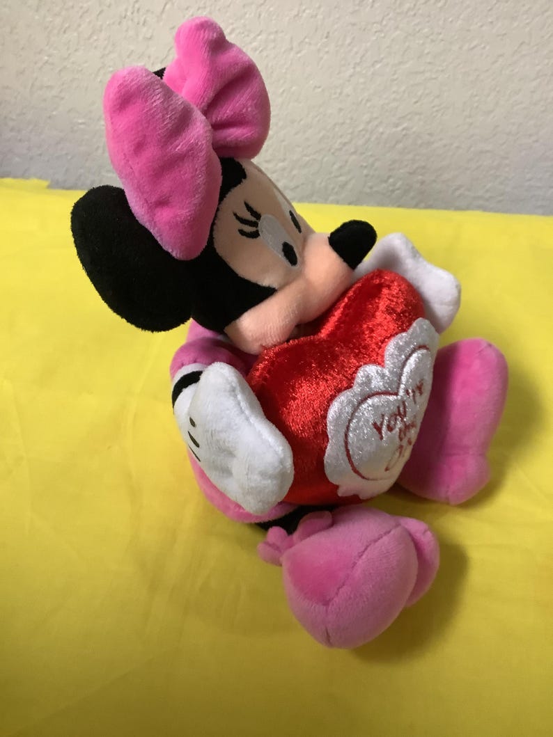 May include: A plush Minnie Mouse toy holding a red heart that says "You're My Valentine". Minnie is wearing a pink bow and a pink dress.