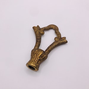May include: A gold-toned metal lamp finial with a decorative antler design.