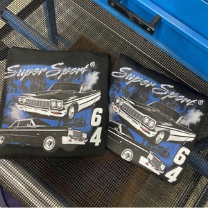 以下が含まれることがあります： ヴィンテージカーと「スーパー・スポーツ64」の文字が描かれた、青と白のグラフィックデザインが施された黒いTシャツ2枚。