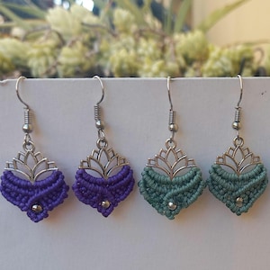 Puede incluir: Un par de pendientes de macramé morado y un par de pendientes de macramé verde con dijes de loto plateados. Los pendientes cuelgan de ganchos plateados.