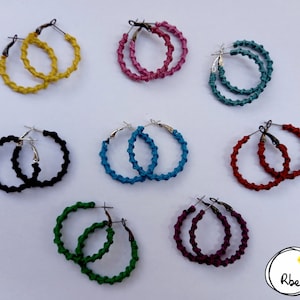 May include: Assortment of ten colourful hoop earrings. The earrings are made of knotted string and have silver hooks. The colours include yellow, pink, teal, black, blue, red, green, and purple.