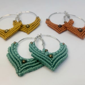 May include: A pair of green macrame hoop earrings with gold beads. The earrings are handmade and feature a chevron design.