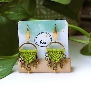May include: A pair of green and gold earrings with a fringe design. The earrings are made with macrame and have a gold hoop and a gold hook.