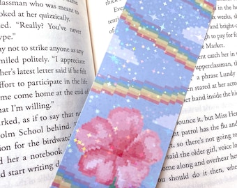 Puede incluir: Un marcapáginas azul y rosa con una flor rosa pixelada y un diseño de rayas arcoíris. El marcapáginas tiene un acabado brillante y estrellas dispersas por el fondo.