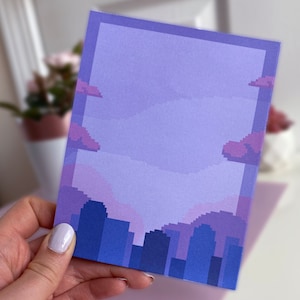 May include: A purple and blue pixel art cityscape with a light purple sky and clouds. The cityscape is made up of tall buildings with flat roofs.