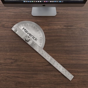 May include: A stainless steel protractor with a pivoting ruler arm, featuring the word Maverick printed in black. The semi-circular head displays degree markings from 0 to 180, while the ruler arm shows metric measurements up to 14 cm.