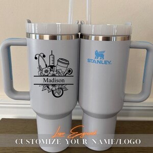 Close-up of a personalized 40oz powder-coated tumbler with a handle and straw. The laser engraving features a custom name in elegant script, a heart-shaped stethoscope design, and motivational nurse affirmations. The tumbler is shown in a professional setting, highlighting its durable finish and large capacity. Perfect gift for nurses and medical staff