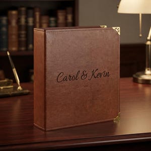 May include: A brown leather-textured binder featuring the engraved text Carol & Kevin on the front cover. The binder includes gold-toned metal corner protectors on the top and bottom right edges, providing a structured appearance for document storage.