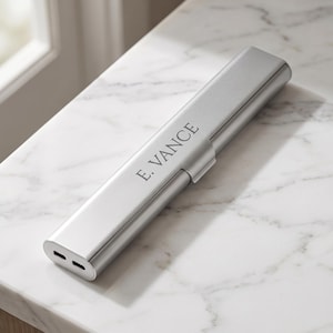 May include: A sleek, rectangular silver metal case with a hinged lid, featuring the engraved text E. VANCE on the top surface. The case has a smooth, metallic finish and two small, horizontal rectangular openings visible on the front end.