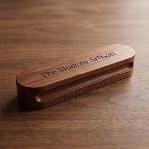 May include: A rectangular wooden block with rounded ends featuring the engraved text The Modern Artisan on the top surface. A horizontal groove runs along the front side, which includes an integrated ruler with markings in inches.