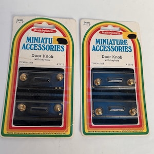Puede incluir: Dos paquetes idénticos de pomos de puerta con cerradura Realife Miniatures, artículo número 804. Cada tarjeta contiene cuatro juegos de pomos en miniatura de tono dorado sobre placas rectangulares negras, con escala de 1 pulgada a 1 pie.