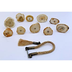 May include: A collection of agate stone cabinet knobs and a rope handle with metal hardware. The knobs are various shapes and sizes, with natural color variations of beige, brown, and white. The rope handle is made of a thick, twisted natural fiber.