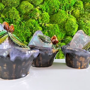 Peut inclure: Trois petits pots en céramique en forme de montagnes avec des feuilles vertes et des baies brunes. Les pots sont émaillés d'une couleur brun foncé et violette avec une finition brillante.