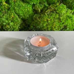 Pode incluir: Um porta-velas de vidro transparente com uma superfície texturizada segura uma pequena vela de chá branca com uma chama a cintilar.