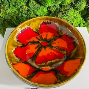 Peut inclure: Un grand bol rond en céramique avec un motif floral. Le bol est décoré d'une grande fleur rouge et orange avec des accents verts. Le bol est glacé d'une finition brillante.