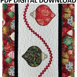 May include: A quilted Christmas table runner with a white center panel featuring two bell-shaped ornaments. The ornaments are red and green with gold accents, and a red, wavy trim runs down the center. The words "PDF DIGITAL DOWNLOAD" are at the top.