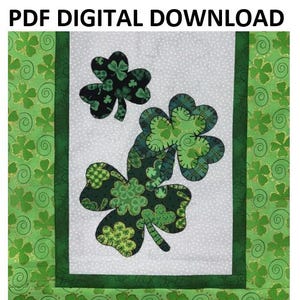 Może przedstawiać: Cyfrowy wzór do pobrania w formacie PDF na blok kołdry w kształcie zielonej koniczyny. Koniczyna jest wykonana z wielu zielonych kawałków tkaniny z dodatkami złotych błyskotek. Tło jest białe z zieloną ramką.