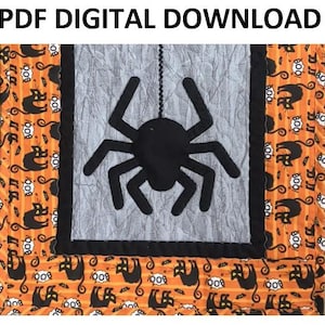 Könnte beinhalten: Ein Halloween-Quilt mit einer großen schwarzen Spinne, die an einer Perlenschnur in der Mitte hängt. Die Spinne befindet sich vor einem grauen Hintergrund, der von einem schwarzen Rand umgeben ist. Die Ränder des Quilts zeigen einen orangefarbenen Stoff mit schwarzen Katzen- und "BOO!"-Mustern. Der Text oben lautet "PDF DIGITAL DOWNLOAD."
