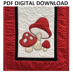 Könnte beinhalten: Ein digitaler PDF-Download-Muster für eine gequiltete Wandbehänge mit drei roten und weißen Pilzen mit weißen Stielen. Die Pilze befinden sich auf einem weißen Hintergrund mit einem gesteppten Wirbelmuster. Der Hintergrund ist mit einem roten Stoff mit weißen Punkten und einem schwarzen Rand gerahmt.