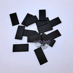 Peut inclure: Un tas de carreaux rectangulaires noirs, éparpillés sur une surface blanche.
