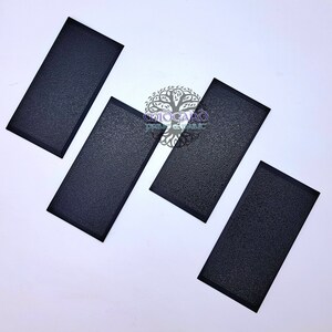 Könnte beinhalten: Vier schwarze rechteckige Klebepads mit einer strukturierten Oberfläche. Die Pads haben einen schwarzen Rand.