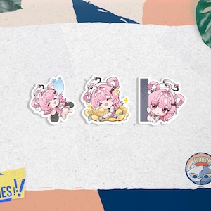 Puede incluir: Tres pegatinas de estilo anime con un personaje de pelo rosa en diferentes poses. Una pegatina muestra al personaje sosteniendo un globo azul, otra muestra al personaje sentado en una pila de monedas de oro, y la última mirando desde detrás de un objeto gris.