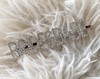 May include: A silver hair clip with the word "BRIDESMAID" spelled out in rhinestones.