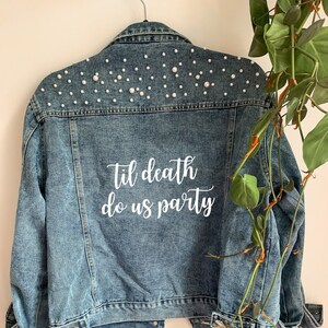 May include: A blue denim jacket with white pearl embellishments on the shoulders and the text "Til death do us party" on the back.