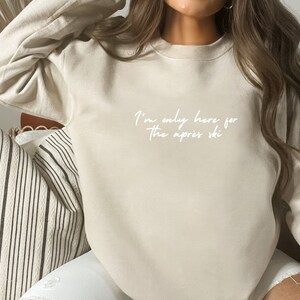 May include: A beige sweatshirt with the text "I'm only here for the apres ski" written in white.