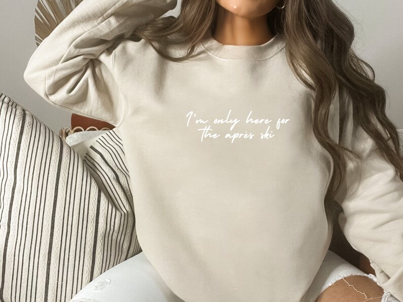 May include: A beige sweatshirt with the text "I'm only here for the apres ski" written in white.