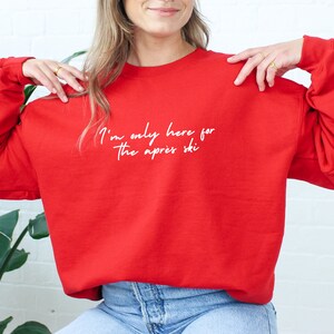 May include: Red sweatshirt with the text "I'm only here for the apres ski" in white.