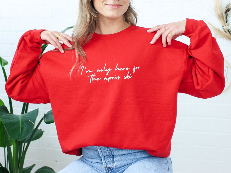 May include: Red sweatshirt with the text "I'm only here for the apres ski" in white.