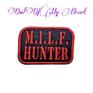 May include: A black and red embroidered patch with the text "M.I.L.F. HUNTER" in red.
