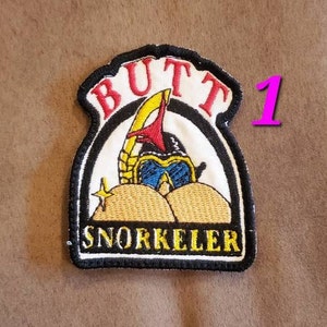 Puede incluir: Un parche bordado en blanco y negro con el texto "Butt Snorkeler" en un c&iacute;rculo blanco con un contorno negro. El parche presenta una imagen de dibujos animados de una persona que lleva un snorkel y una m&aacute;scara de buceo con las nalgas expuestas.